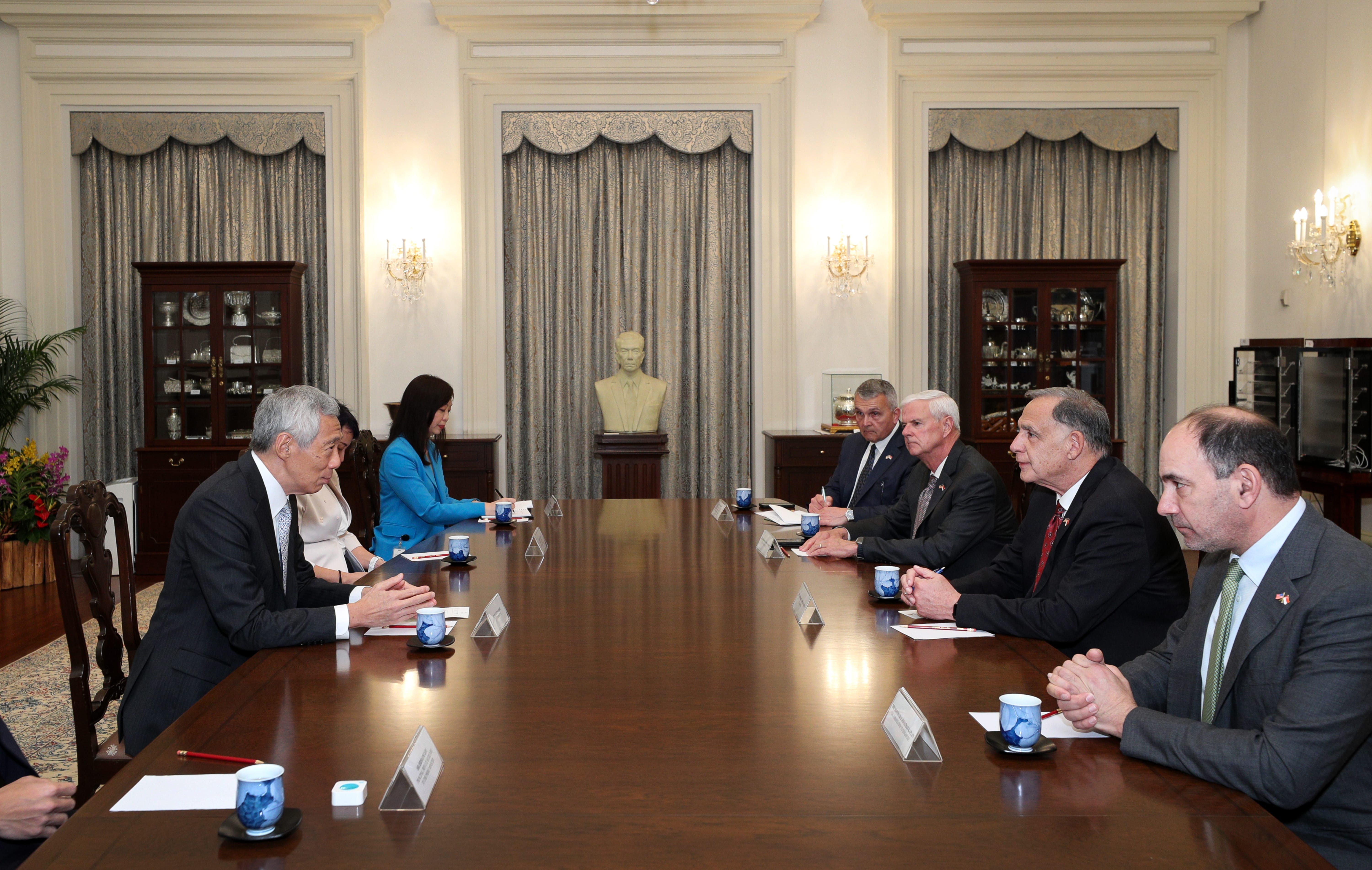 People seated around a long, polished table in a formal room with drapery and display cabinets.